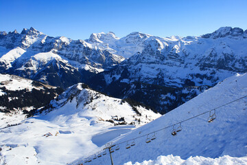 Scenic view of the French Alps with snowy peaks and a chairlift under clear blue sky. Winter...