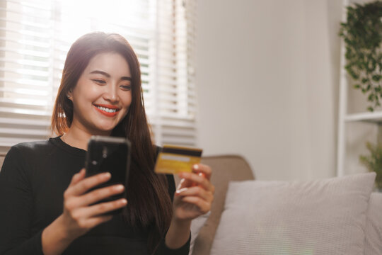 Smiling woman shopping online using smartphone and credit card at home