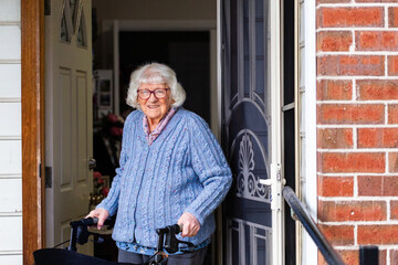 Elderly Australian woman with walker mobility aid standing by front door of home