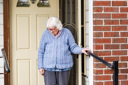 ninety-nine year old woman standing by front door of home looking down holding onto handrail