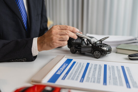 A businessman in a suit is presenting car insurance and contract documents with miniature car models on the desk, symbolizing vehicle insurance, financial planning, and legal agreements. - Powered by Adobe