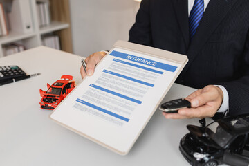 A businessman in a suit is presenting car insurance and contract documents with miniature car models on the desk, symbolizing vehicle insurance, financial planning, and legal agreements.