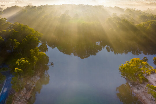 Aerial view of rays of sunshine through fog over gumtrees along the Murray River at Moama