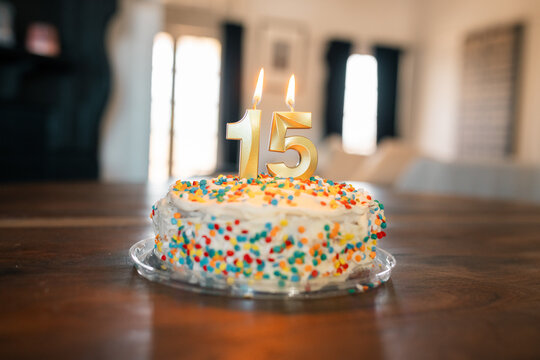Basic birthday cake at home with lit gold 15 candles