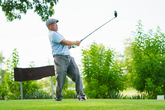 Asian elderly male golfer hitting fairway shot on golf course with sunlight and nature. Sport, leisure and lifestyle.