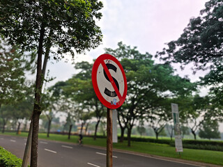 Photo of a traffic no parking sign with a background of urban road and shady trees.
