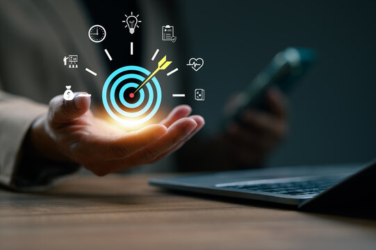 Businesswoman's hand presents glowing target icon, symbolizing business objective, corporate goals, success. Virtual interface displays icons strategy, planning, finance, health, time management, - Powered by Adobe