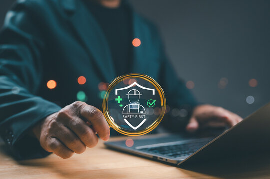 Businessman holding magnifying glass focuses virtual safety first icon, signifying workplace health, protection, industrial regulation, standards compliance. Business security concept highlights