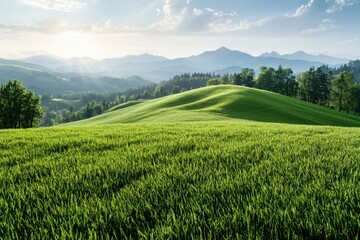 Obraz premium Rolling hill covered with vibrant green grass under bright sky with sun rays shining through clouds, surrounded by distant mountains and trees creating peaceful natural scene