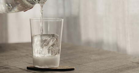 Pour tonic over clear ice cube in tumbler glass on black oak table