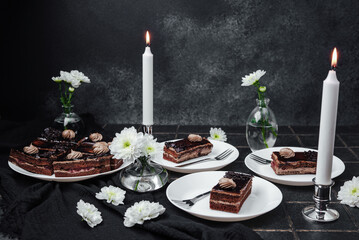 Dark chocolate cake slices on plates with white flowers and lit candles on table