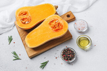 Halved butternut squash on board with rosemary, salt, oil, and peppercorns