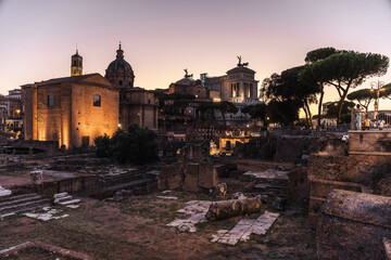 Fototapeta premium Roman Forum ruins with illuminated historical buildings and monuments at dusk in Rome, Italy