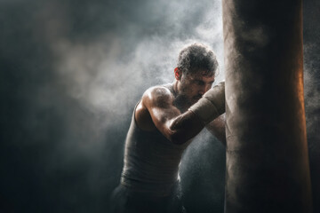 Obraz premium Powerful Boxer Striking Heavy Bag with Dust in Motion