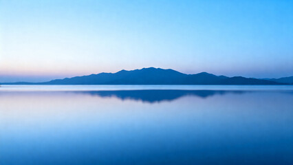 Fototapeta premium Calm lake reflecting distant mountains under a clear twilight sky