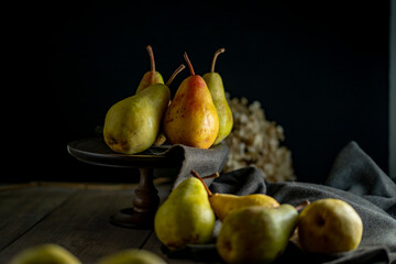 Still Life with Pears on Dark Background.A moody and rustic still life photograph featuring ripe pears against a dark background. The dramatic lighting creates a warm, classic atmosphere. © Tsurukame Design