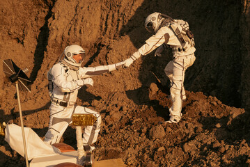 Teamwork of astronauts symbolized by one reaching hand to another on Mars.