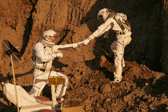 Teamwork of astronauts symbolized by one reaching hand to another on Mars.