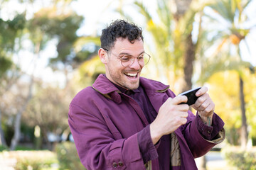 Fototapeta premium Young caucasian man at outdoors playing with the mobile phone