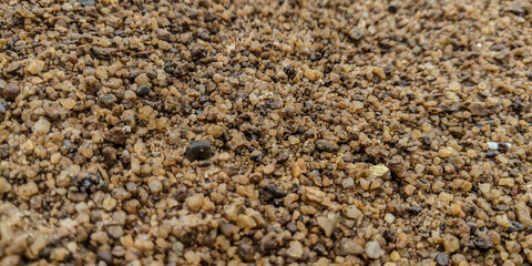 Close-up of coarse brown sand texture, natural construction material used for building, mixing concrete, and landscaping.