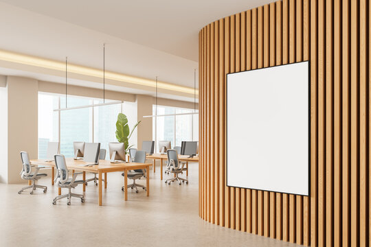 Modern office interior with vertical wood slat wall and blank poster mockup in open workspace with desks and computers near large windows during daytime. 3D Rendering