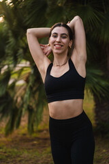 Fototapeta premium Young woman smiling doing arm stretching outdoors