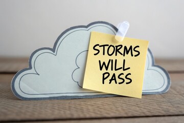 Inspirational quote on sticky note attached to a paper cloud symbolizing hope during difficult times on a wooden surface