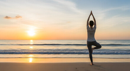 Woman practicing yoga tree pose on beach at serene golden sunrise