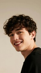 Portrait of a young man with curly hair smiling warmly against a neutral background