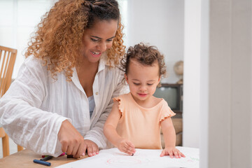 Enjoy happy smiling love family. Mother with little girl learning and writing in book with pencil making homework at home. Education concept	