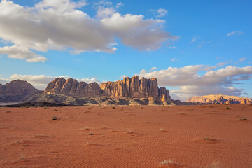 Wadi Rum desert with red sand lit by evening sun, rocky mountain formations in background