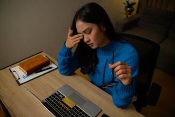 Woman feeling tired and stressed, rubbing her eyes from eyestrain after prolonged laptop use while holding credit card for online shopping