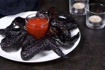 Vampire Wings (Chicken Wings) Cooked in sweet and sour sauce with cuttlefish ink, served with ketchup on a plate. An original idea for a Halloween party