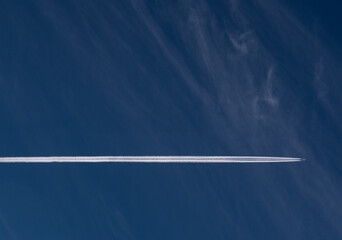 Vapor trail agains blue sky and fleece clouds