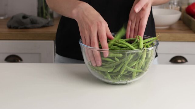 hands put green beans in bowl on table