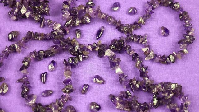Amethyst bead necklace lies on a purple cloth, top view, rotation, background