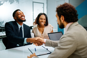 Happy couple concluding a loan agreement with a financial advisor, shaking hands in an office