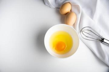 Ingredients for making a simple omelet. A raw egg in a plate, a whisk for beating on a white background.