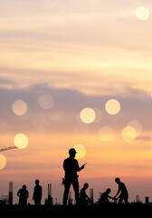 Fototapeta premium Silhouette of Construction Workers at Sunset with Crane and Bokeh Lights