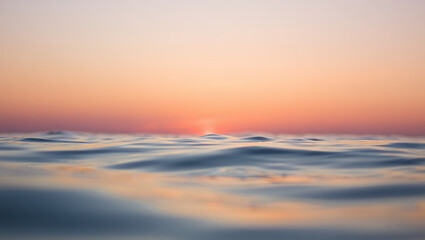 Obraz premium Gentle ocean waves reflect the soft hues of a pastel sunset, creating a serene and tranquil atmosphere