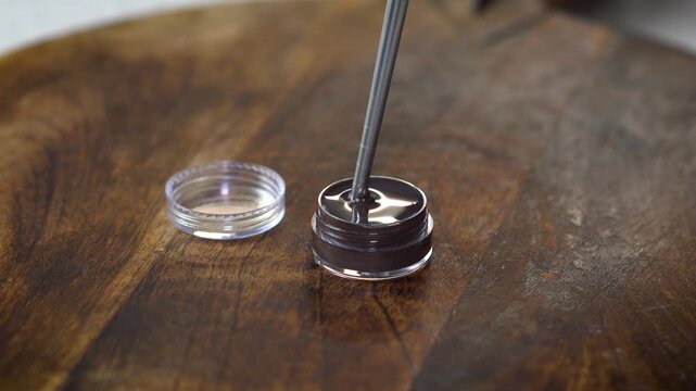 Checking the consistency of natural homemade lip balm in small transparent container. DIY organic skincare, eco-friendly beauty, artisanal cosmetics, and handcrafted sustainable style.
