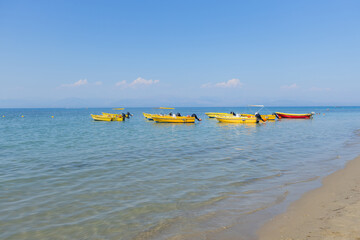 Fototapeta premium Tranquil scene of a calm, sandy beach with a line of yellow rental boats floating in the clear blue water under a bright summer sky