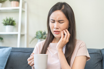 Suffering from toothache, hurt asian young woman touch cheek, face expression ache or feel pain, sensitive molar teeth, hand holding glass of water with ice, inflammation when drink cold, healthcare.