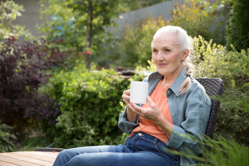Obraz premium portrait of a cheerful elderly woman with a cup of tea in the garden about her home on a summer. concept without stress. mental health. Enjoying the little things. Mindfulness and feel-good moments.