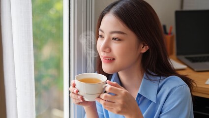 Young Woman Enjoying Warm Tea While Looking Out of Window with a Peaceful Expression at Home