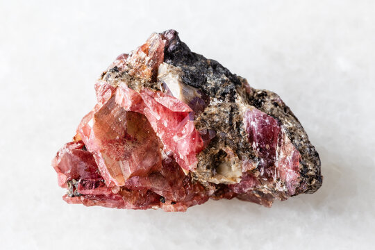 sample of raw rhodonite mineral on white marble