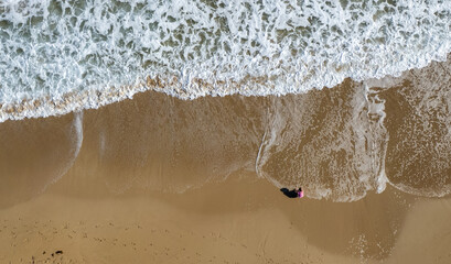 Aerial drone point of view of person walking on sand in a beach. Stormy waves idyllic beach in winter.