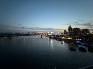 Evening panoramic view of Oktoberfest in Cincinnati, Ohio, with crowds gathered along the riverfront steps, illuminated tents, and boats floating on the Ohio River.