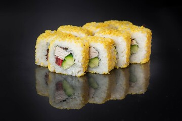 Sushi rolls arranged neatly on a reflective black surface. The rolls are coated with a golden crispy layer and contain cucumber and fish.