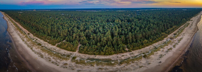 A stunning aerial view of a serene forest sandwiched between two vast bodies of water, bathed in the soft hues of sunset